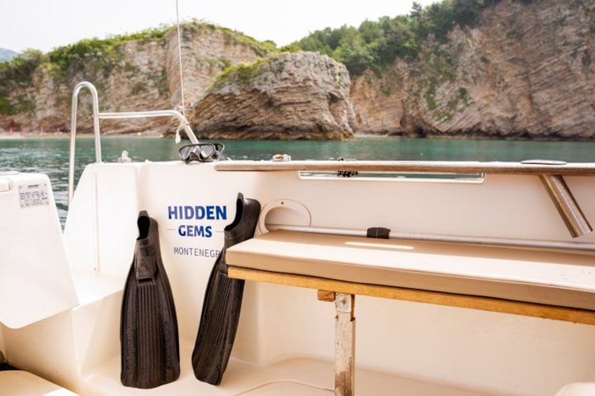Una barca con un cartello 'Hidden Gems Montenegro', una panca di legno e scogliere rocciose sullo sfondo. 3