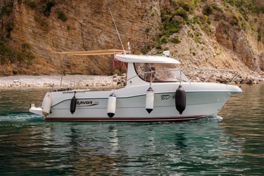 Una barca bianca con la scritta 'AVOR' sul fianco, che galleggia in acque calme con una costa rocciosa sullo sfondo. 1