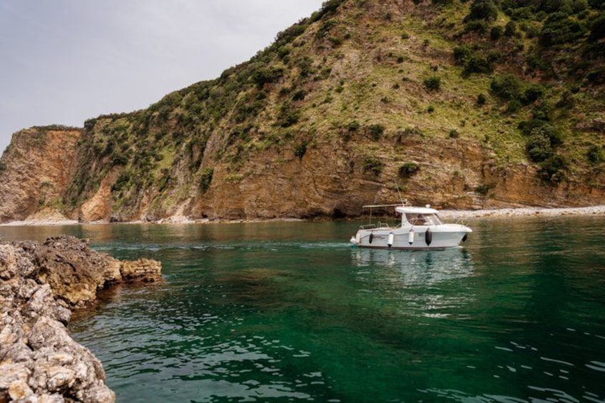Una barca su acque calme, con una costa rocciosa e una collina sullo sfondo. 4