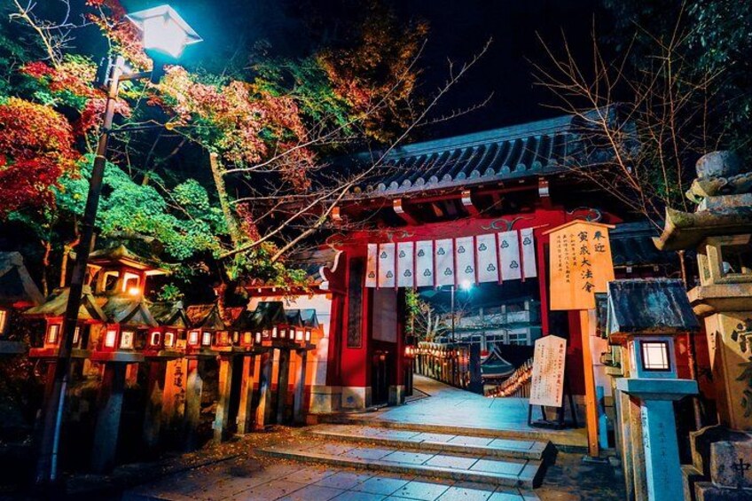 En traditionel japansk torii-port om natten, omgivet af oplyste lanterner og træer i efterårsfarver. 2