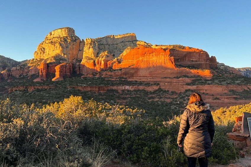 Une personne se tient debout dans un paysage naturel, avec des formations rocheuses rouges et une végétation verdoyante. 5