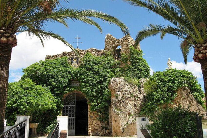 A historic building with a cross on top, surrounded by lush greenery and palm trees. 1
