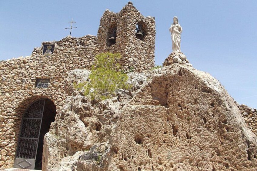 A stone church with a statue on top, a bell tower, and a cross. 5