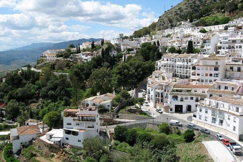 A hillside town with white buildings, a winding road, and a mountainous backdrop. 2