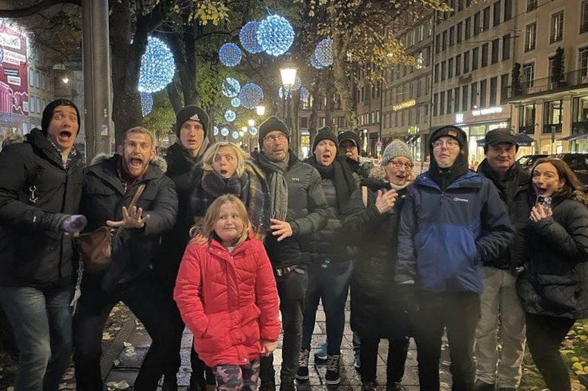 A group of people standing on a city street at night with illuminated decorations in the background. 3