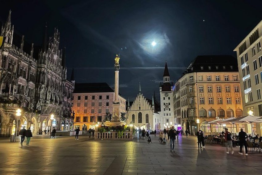 A nighttime city square with historic buildings, a prominent tower, and a statue. 1