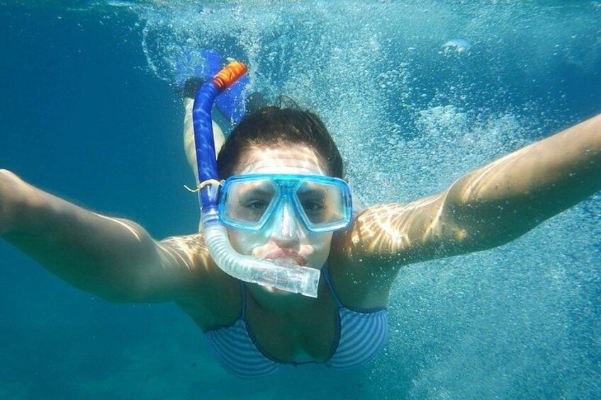 Una persona bajo el agua, con snorkel y máscara, nadando en aguas cristalinas azules. 1