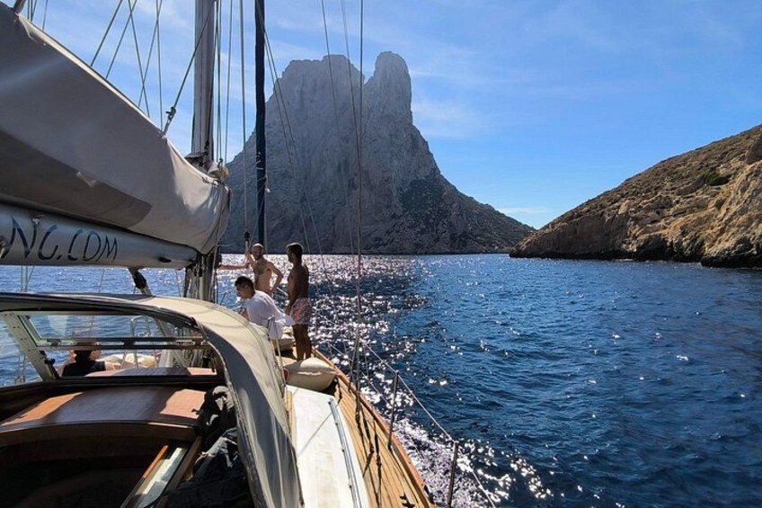 Un velero en aguas tranquilas con una costa rocosa y un acantilado imponente al fondo. 4