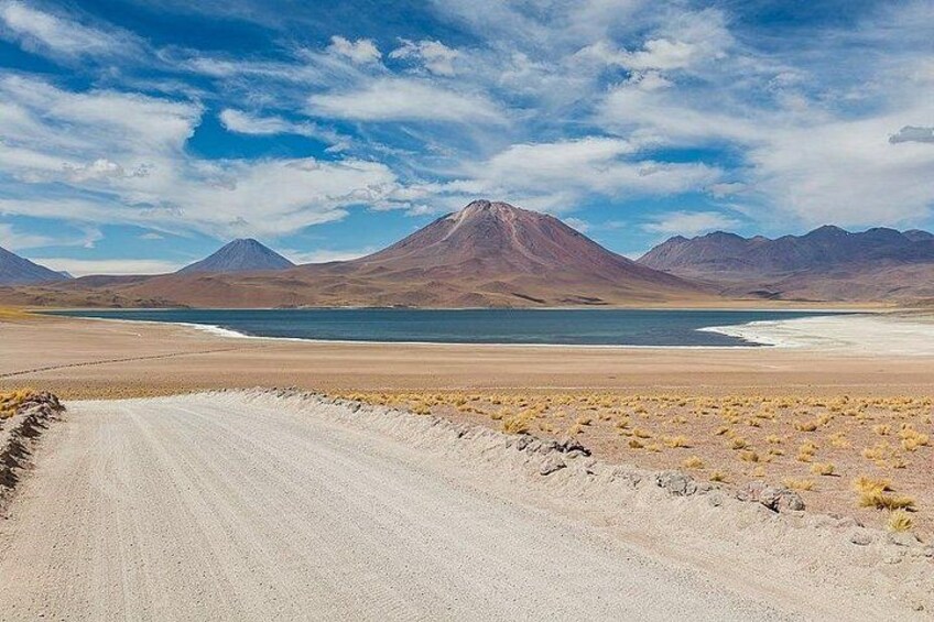 Paesaggio desertico con una strada sterrata, un lago e montagne sullo sfondo. 1