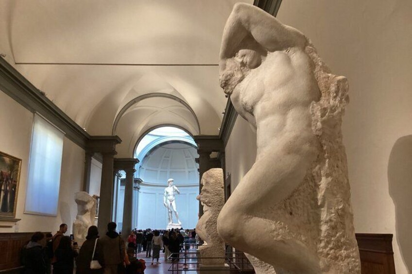 A museum interior with classical sculptures and a large arched window. 3