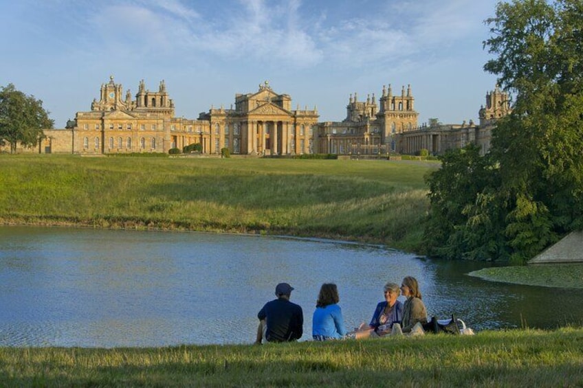 A large historic building with a pond and people sitting by the water. 2