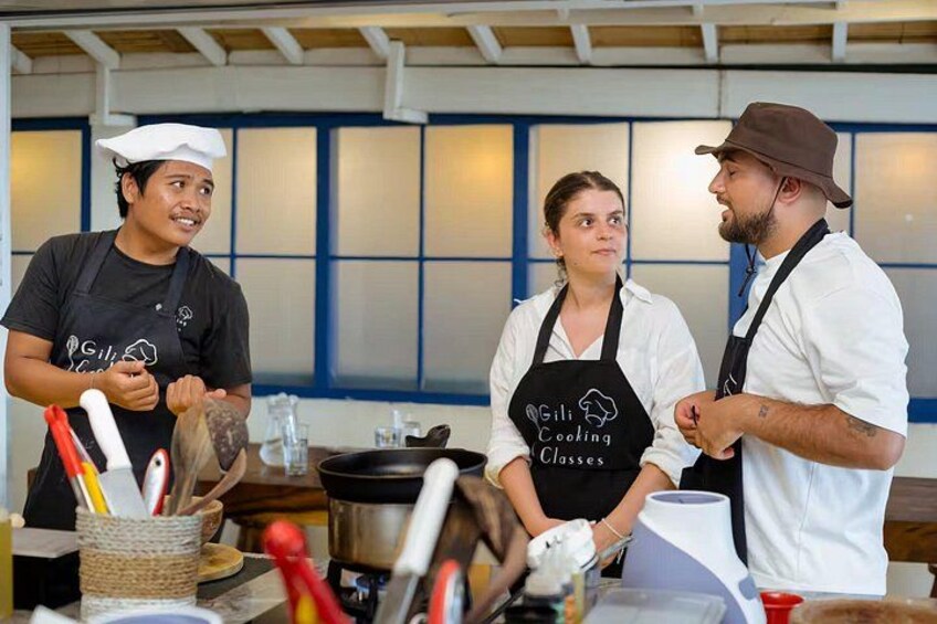 Three people in a kitchen, wearing aprons, with cooking utensils and a pot on the counter. 5