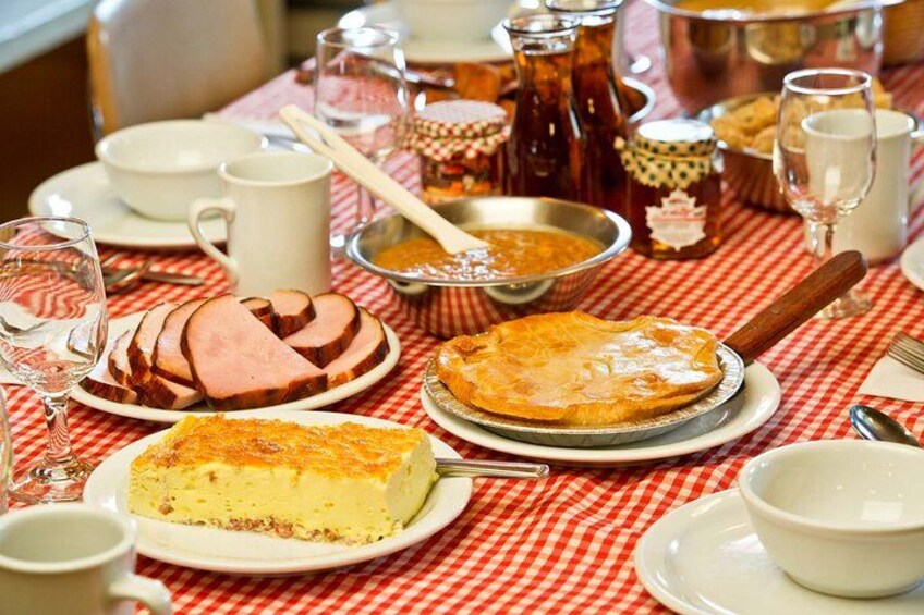 A table set with various dishes including a pie, ham, and a cheesecake, along with cups and a pitcher. 3