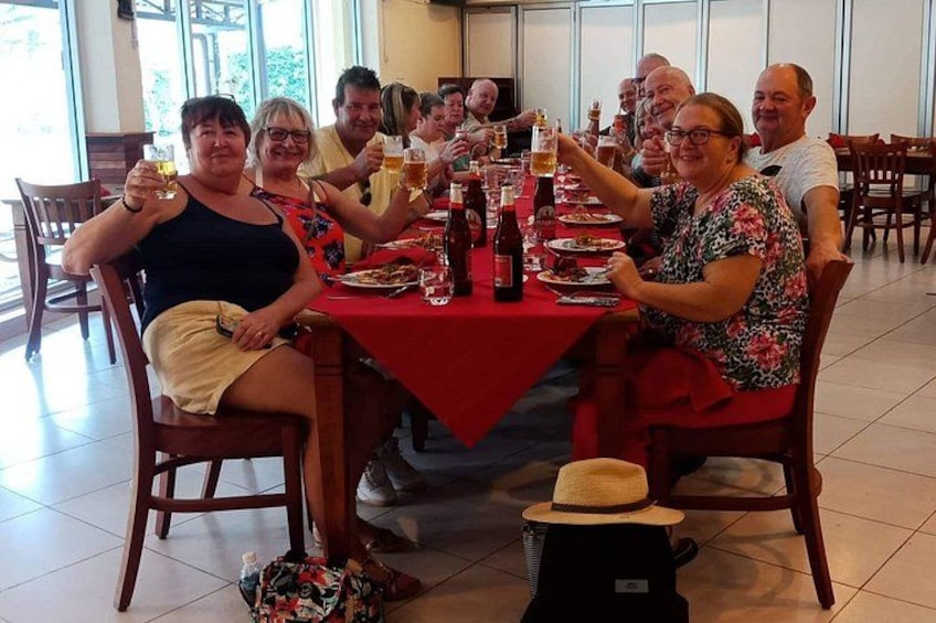 A group of people sitting around a table with drinks, plates of food, and a red tablecloth. 1