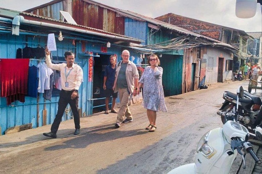 A street scene with people walking, a motorcycle parked, and buildings with corrugated metal roofs. 3
