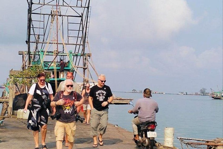 A group of people walking and riding a motorcycle on a dock by a body of water. 5