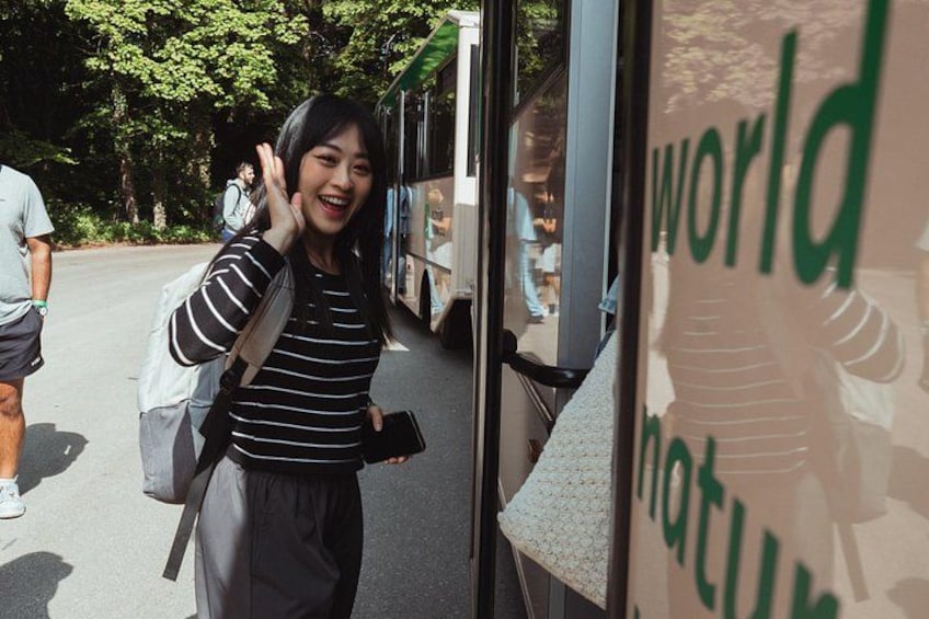 A person standing next to a bus with a backpack, a mobile phone, and a bag. 2