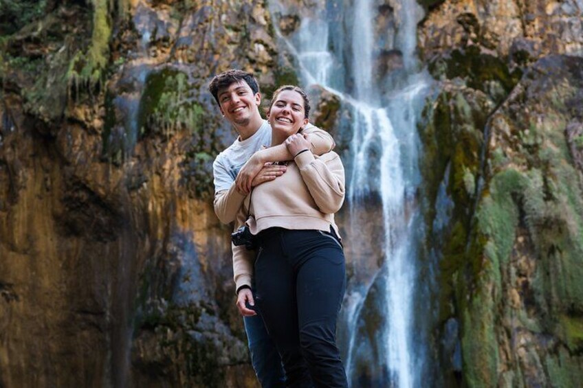 A couple embracing in front of a waterfall with moss-covered rocks. 5