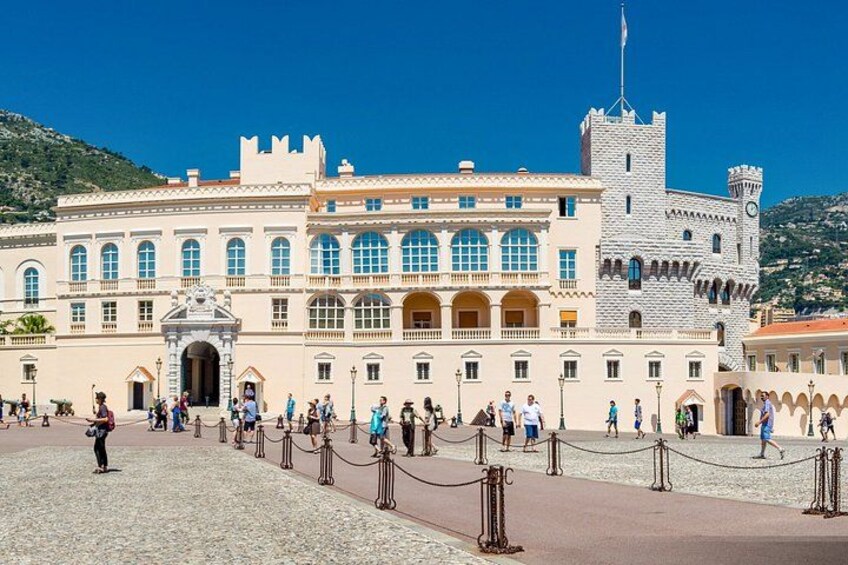 Un edificio storico con una torre simile a un castello, un ampio cortile aperto e persone che passeggiano. 2