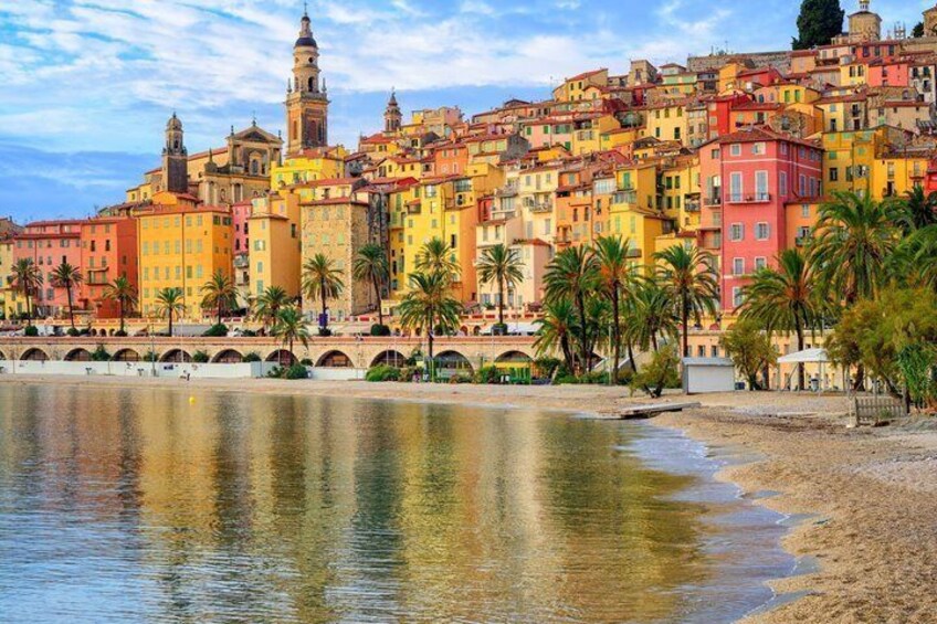 A coastal cityscape with colorful buildings, a beach, and palm trees. 1