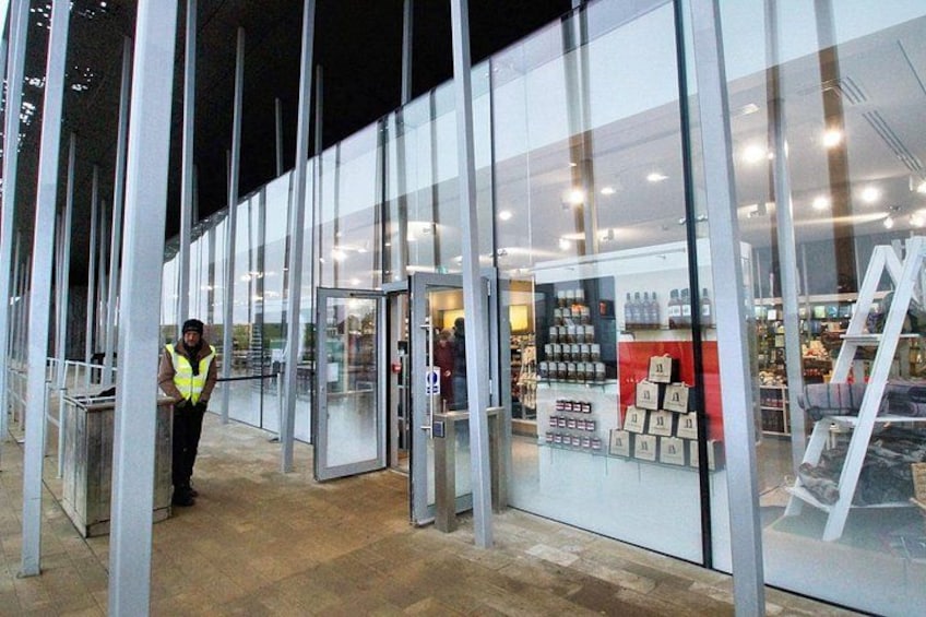 A modern building with glass doors and a person in a high-visibility vest standing outside. 5