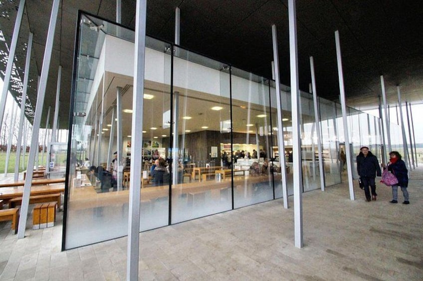 A modern building with large glass windows and a seating area outside. 2