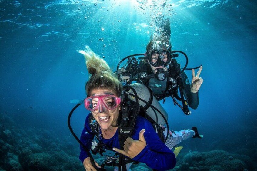 Two scuba divers underwater with bubbles and a coral reef in the background. 1