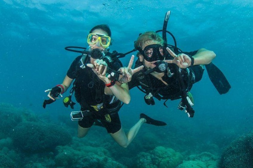 Two scuba divers underwater with scuba gear, making peace signs. 4