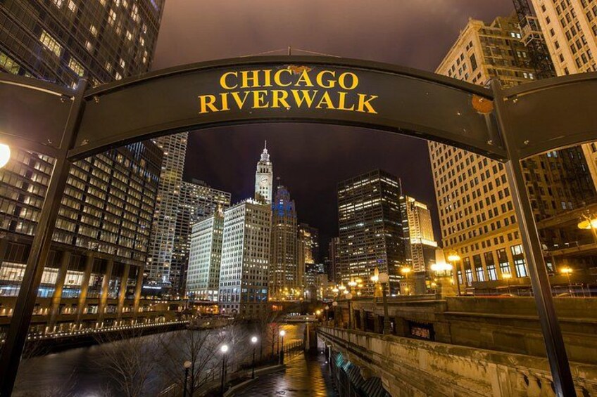 Panorama nocturno de la ciudad con el cartel del Chicago Riverwalk, edificios iluminados y el río. 3