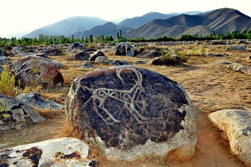A large rock with ancient carvings in a desert landscape with mountains in the background. 1