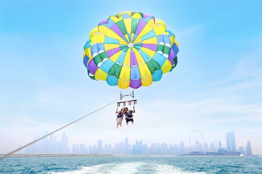 Une personne pratiquant le parachute ascensionnel au-dessus de l’eau, avec un parachute aux couleurs vives, une vue sur les gratte-ciel d’une ville en arrière-plan et une grande roue. 3