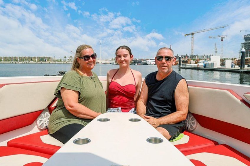 Trois personnes se trouvent sur un bateau, avec une marina et des grues en arrière-plan. 5