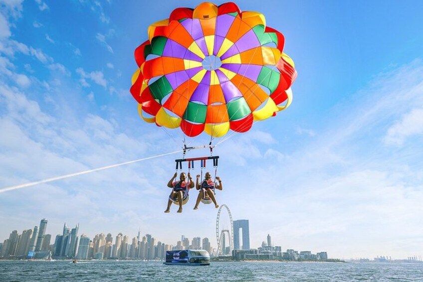 Une activité de parachute ascensionnel avec un parachute aux couleurs vives au-dessus de l’eau, une vue sur les bâtiments d’une ville en arrière-plan et une grande roue. 4