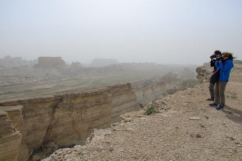 A canyon with a deep vertical drop, a rocky ledge, and a distant building. 1