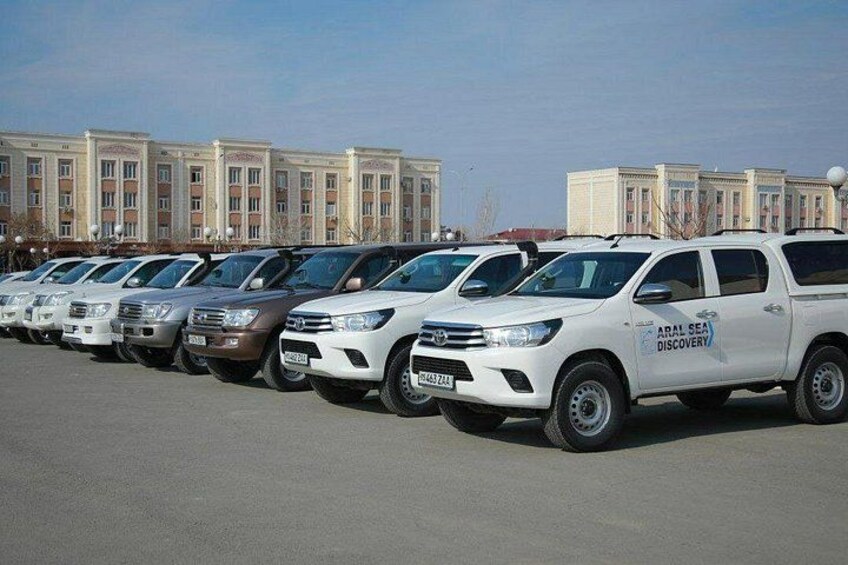 A row of white SUVs parked in a lot with a building in the background. 4
