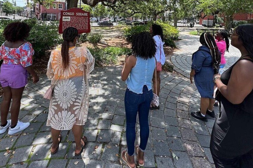 A group of people standing on a paved path in a park with a sign reading 'Congo Square'. 5