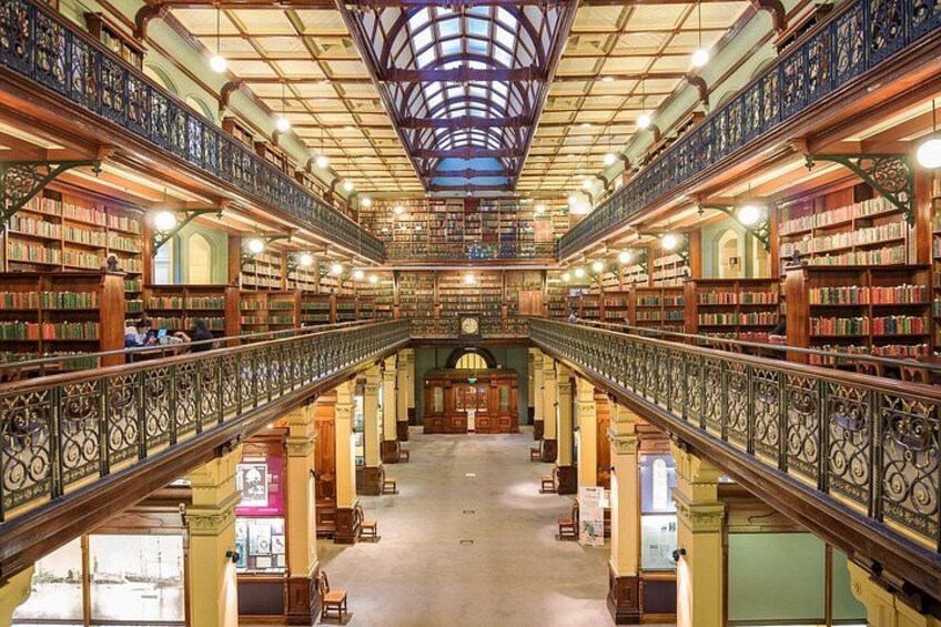 Una biblioteca imponente y ricamente decorada, con techos altos, intrincadas barandillas de hierro y estanterías repletas de libros. 1