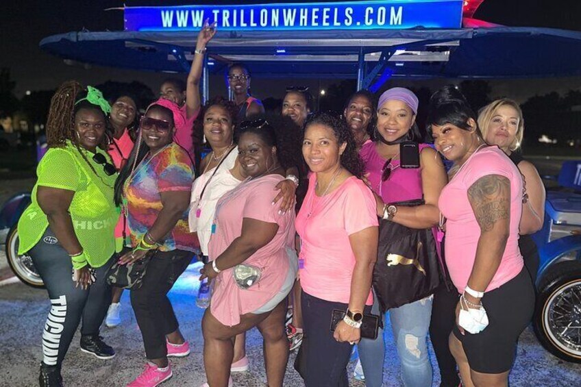 A group of people posing in front of a vehicle with a sign that reads "WWW.TRILLONWHEELS.COM". 1