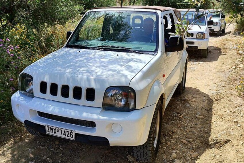 A white SUV parked on a dirt path with vegetation on the sides. 2