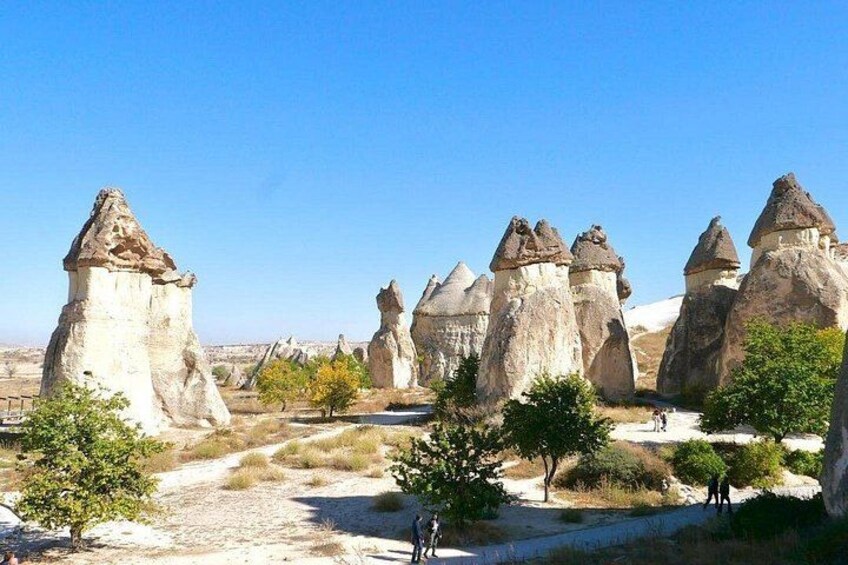 A landscape with unique rock formations, a clear sky, and a few people walking. 3
