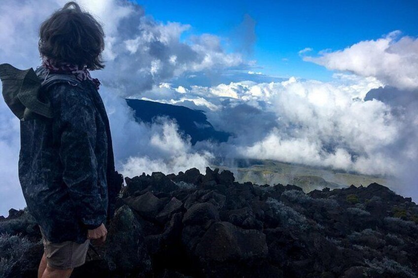 Una persona de pie sobre un afloramiento rocoso, con vista a un paisaje montañoso y nubes abajo. 3