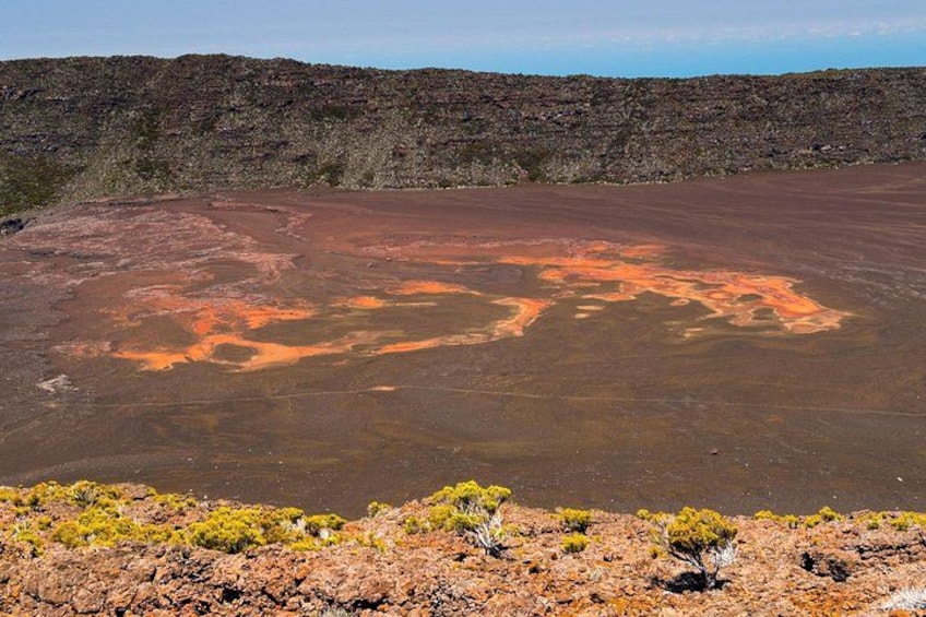 A barren landscape with a large, flat, reddish-brown area with orange patches, surrounded by rocky terrain and sparse vegetation. 2