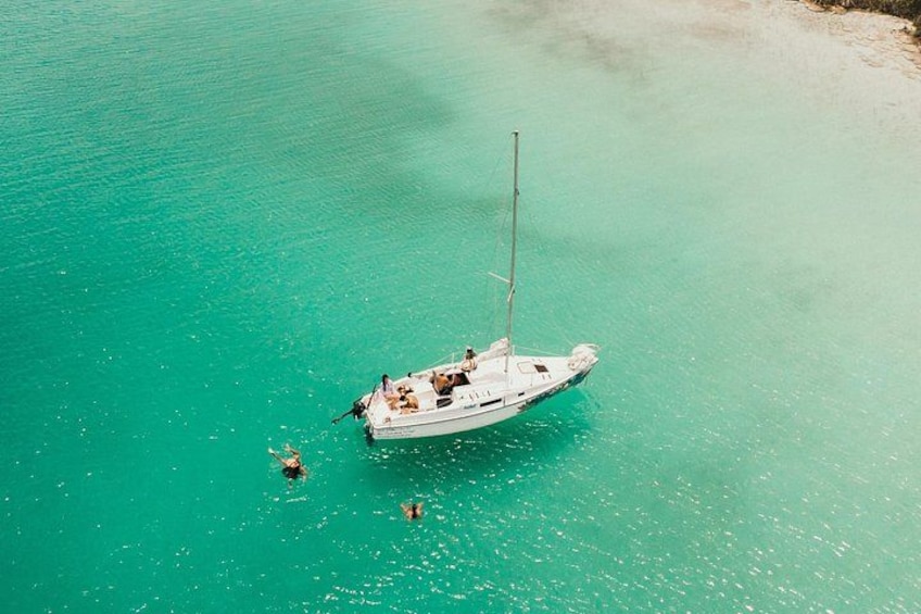 A sailboat anchored in clear turquoise water with a sandy beach in the background. 4