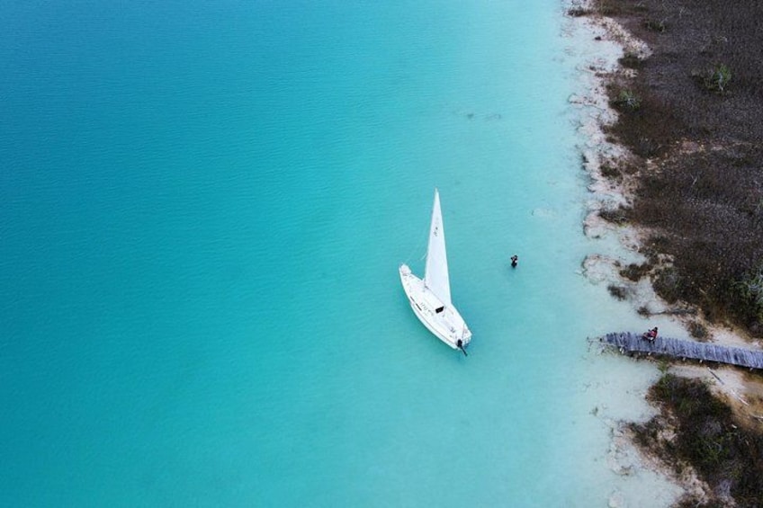 A sailboat on turquoise water near a beach with sparse vegetation. 2