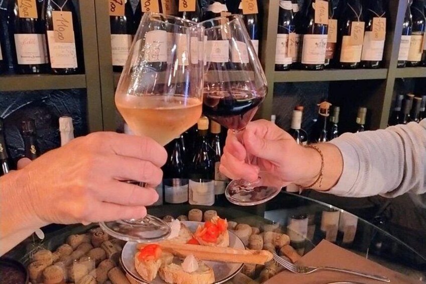 Two people toasting with wine glasses, a bottle of wine, and a plate with food on a table. 2