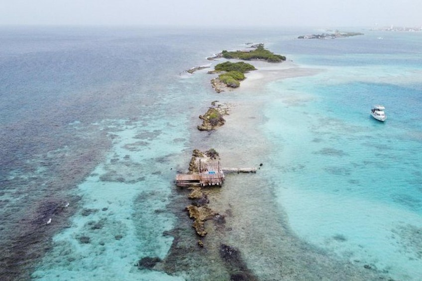 An aerial view of a coastal area with clear turquoise waters, a small boat, and a dock extending into the sea. 4