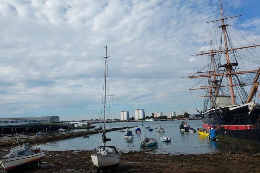 Ein Hafen mit einem großen Segelschiff, einigen kleineren Booten und einer Stadtkulisse im Hintergrund. 2
