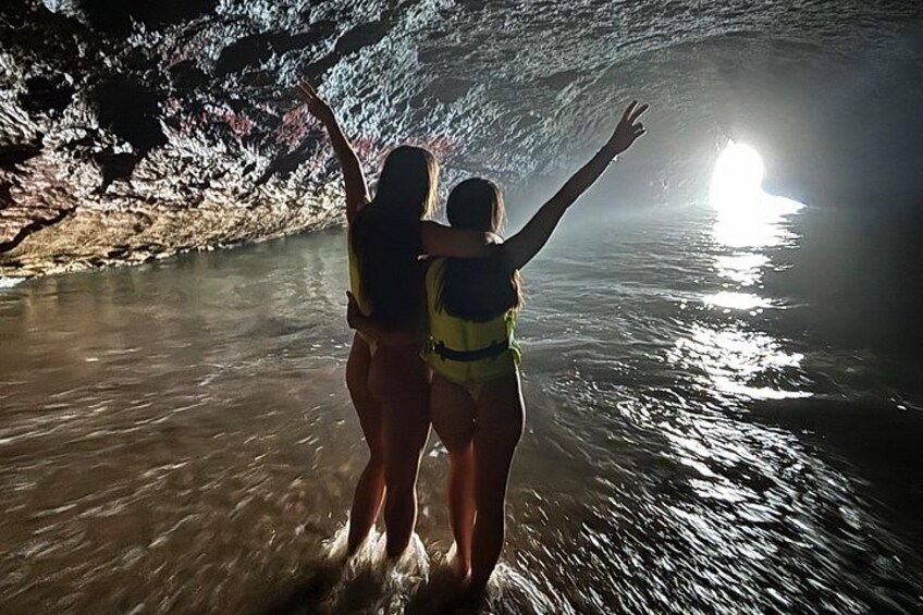 Deux personnes se tiennent dans une grotte, les bras levés, et regardent l’eau. 2