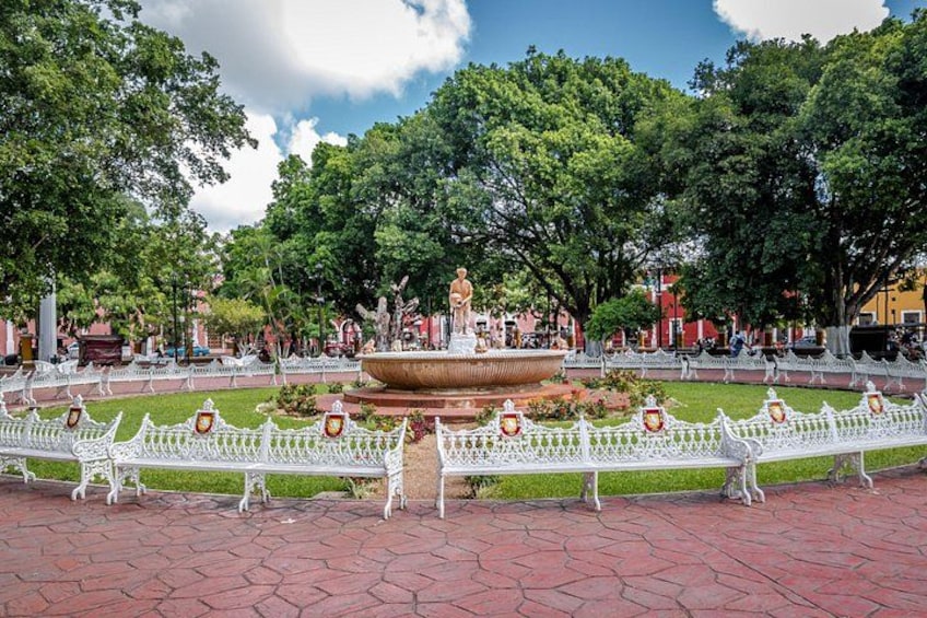 Un parque con una fuente central, rodeado de bancos blancos y una cerca blanca. 2