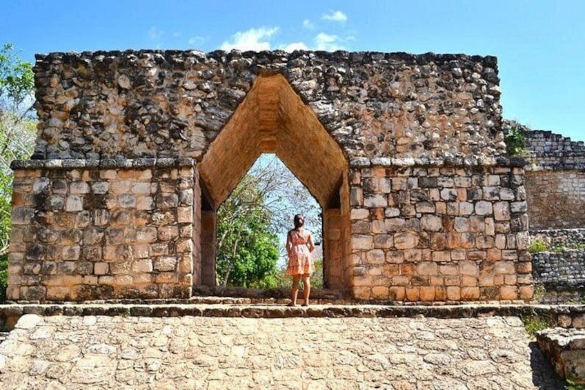 Una estructura de piedra con un arco de entrada, una persona vestida y un cielo azul despejado. 1